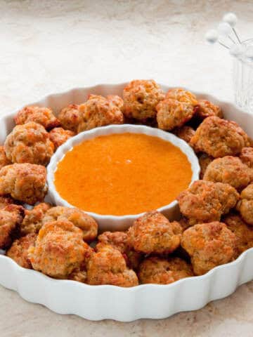 A white serving dish holds the Easy Cheesy Sausage Balls and dthe Apricot dipping sauce.