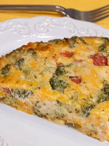 A slice of the Basic Low Fat Quiche Recipe sits on a white plate with a yellow napkin and fork in the background.
