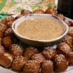 Pretzel bites surround a bowl of Hot Honey Mustard dip with napkins in the background on bottles of beer on the side.