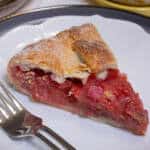 A slice of the Strawberry Rhubarb Galtette sits on a white plate with a fork on the plate.