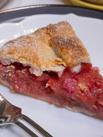 A slice of the Strawberry Rhubarb Galtette sits on a white plate with a fork on the plate.