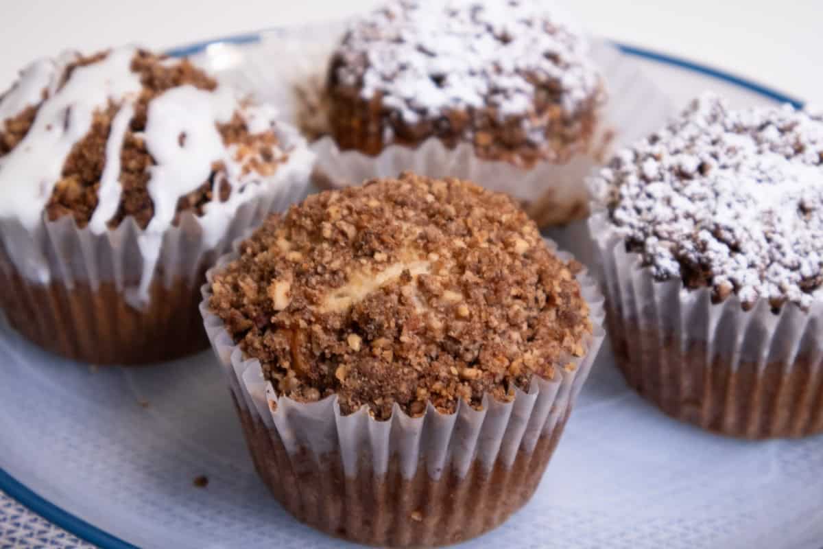 A plate of Banana Streusel Muffins plain, dusted with powdered sugar and drizzled with vanilla drizzle. 