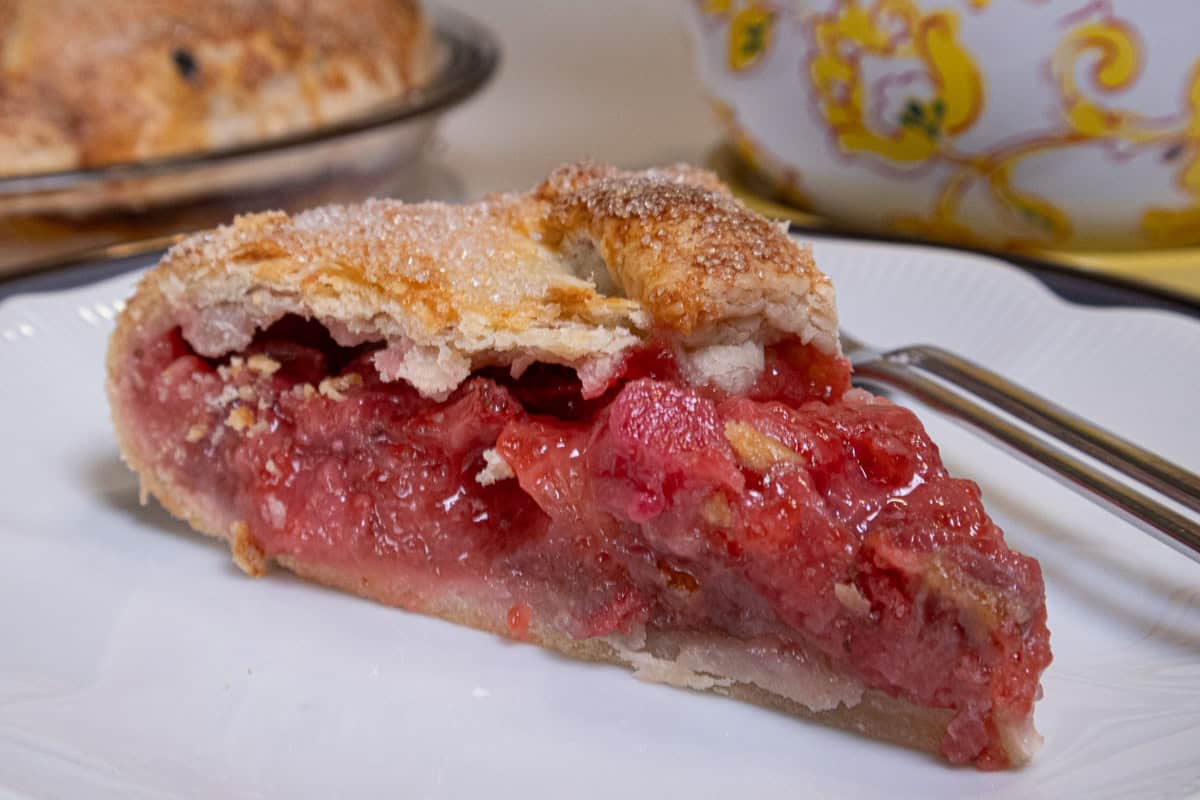 A slice of the Strawberry Rhubarb Galtette sits on a white plate with a fork on the plate.
