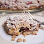 A slice of the Strawberry Crumb Tart on an antique plate with a fork and the tart in the background.