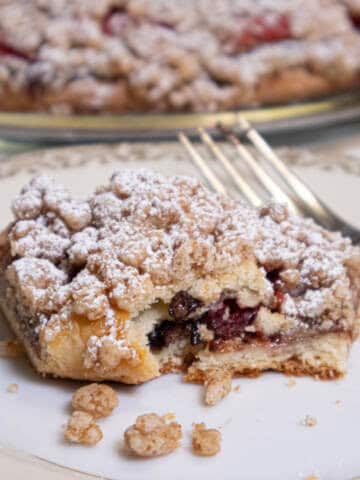 A slice of the Strawberry Crumb Tart on an antique plate with a fork and the tart in the background.