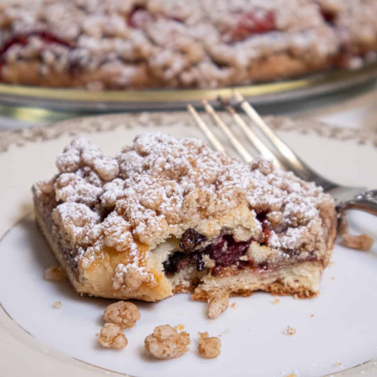 A slice of the Strawberry Crumb Tart on an antique plate with a fork and the tart in the background. 