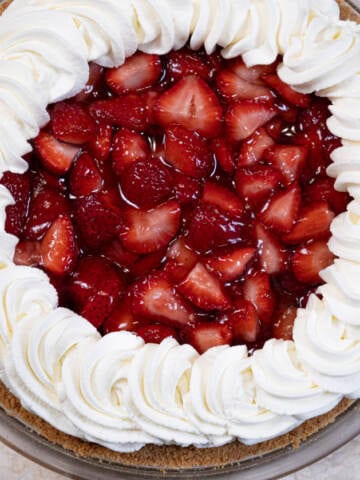 The (almost) No bake Strawberry Pie is seen in the pie plate with a wreath of whipped cream and fresh strawberries.