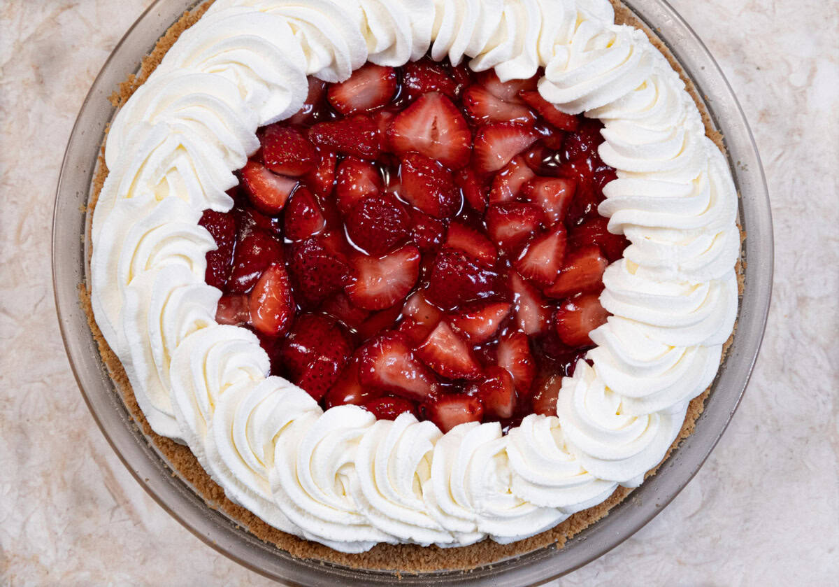 The (almost) No bake Strawberry Pie is seen in the pie plate with a wreath of whipped cream and fresh strawberries.