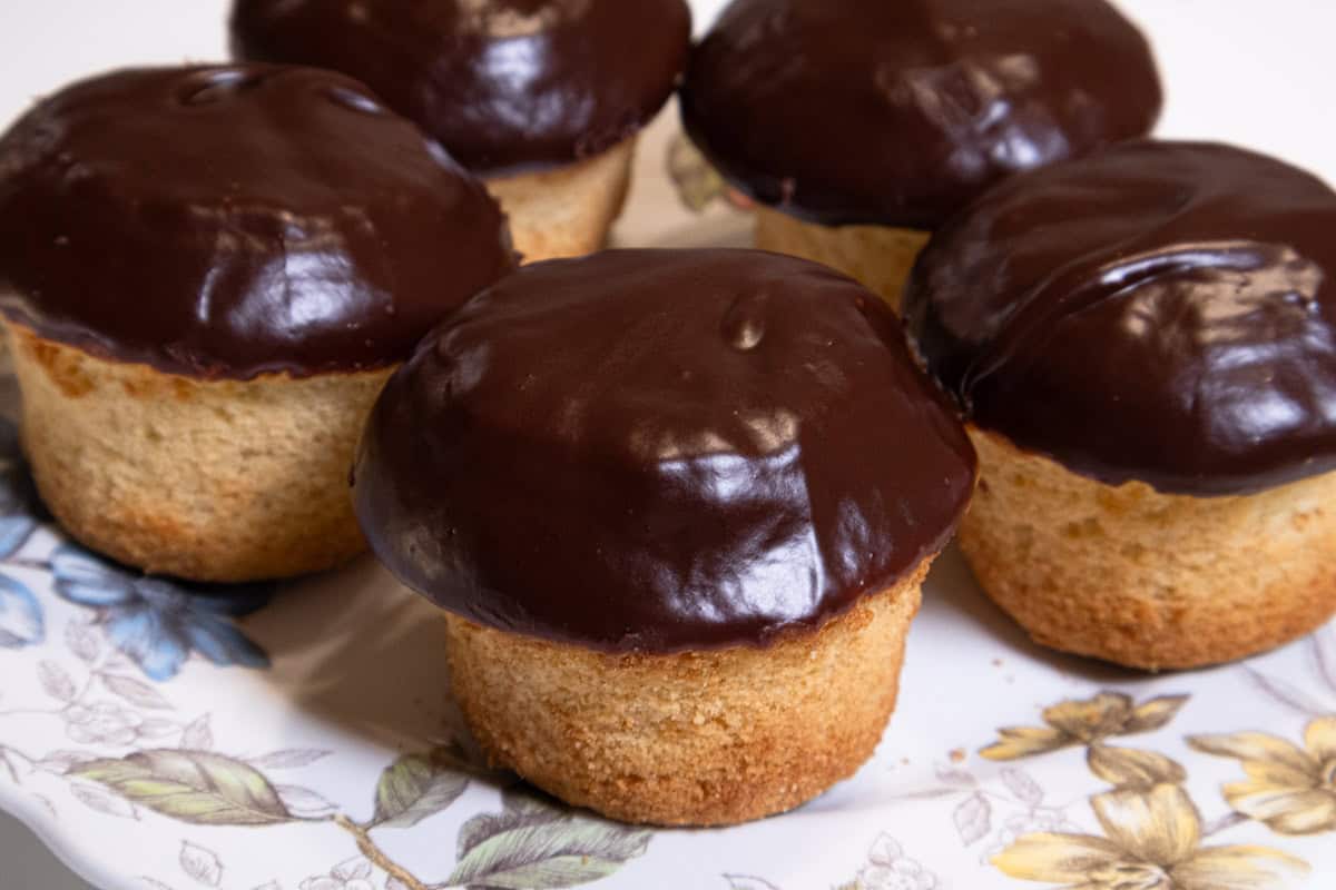 Boston Cream Cupcakes sit on a plate edged with flowers and leaves.