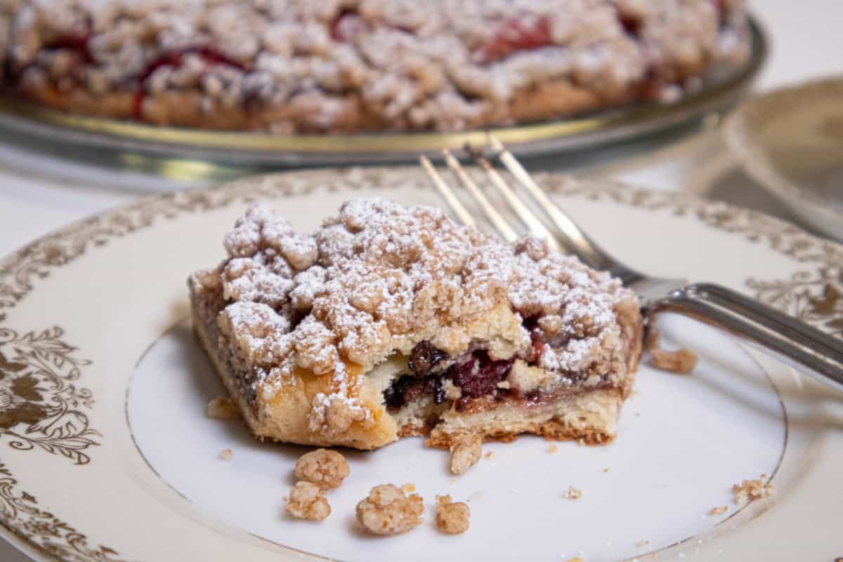 A slice of the Strawberry Crumb Tart on an antique plate with a fork and the tart in the background.