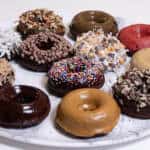 Chocolate Cake Donuts are featured with 12 different toppings sit on a marble platter.