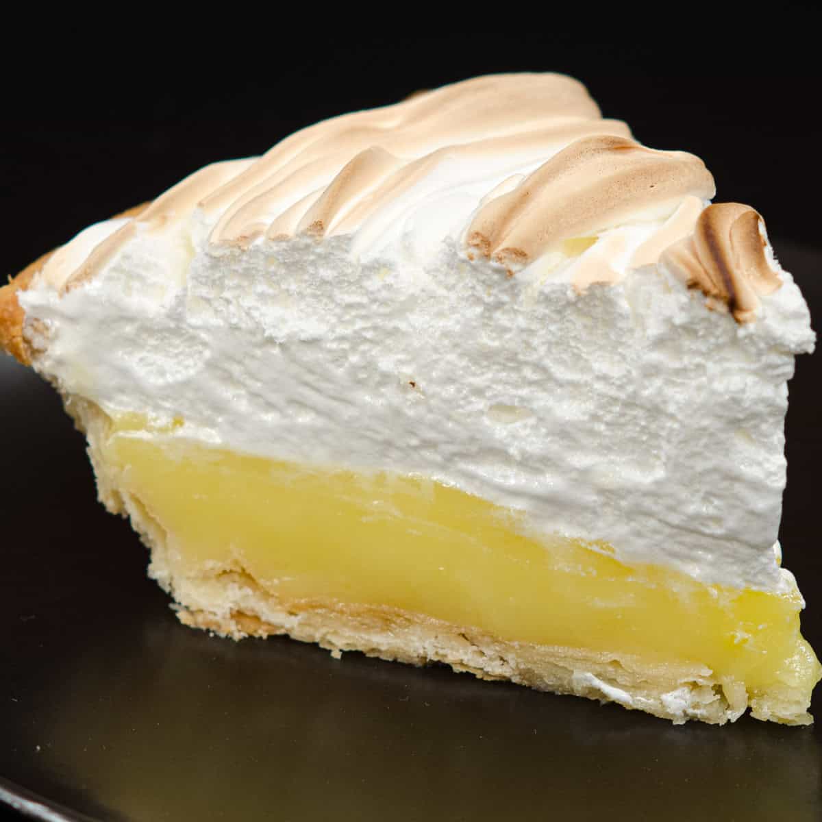 A slice of Lemon Meringue Pie sits on a black plate.