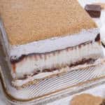 The S'Mores Ice Cream Cake sits on a gold rimmed cake plate with shards of graham cracker crumbs and chocolate around it,