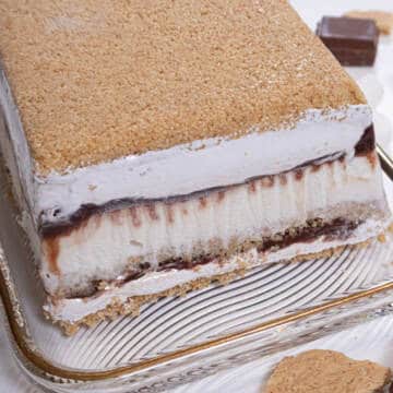 The S'Mores Ice Cream Cake sits on a gold rimmed cake plate with shards of graham cracker crumbs and chocolate around it,