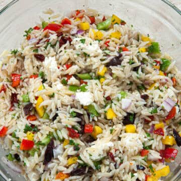 A close up photo of the Mediterranean Orzo Salad shows the cut up veggies, olives and cheese surrounding the orzo pasta.