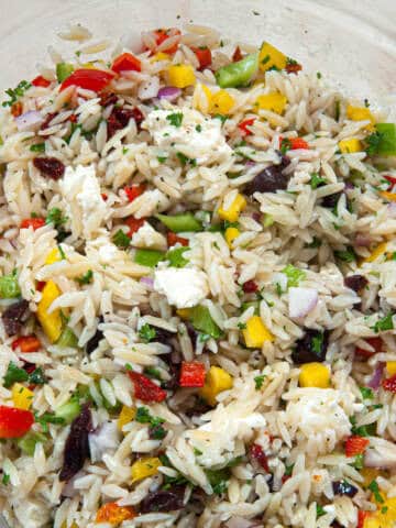 A close up photo of the Mediterranean Orzo Salad shows the cut up veggies, olives and cheese surrounding the orzo pasta.