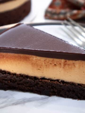 A slice of the Chocolate Peanut Butter Mousse Cake sits on a marlbe plate with the cake in the vackground along with a napkin.