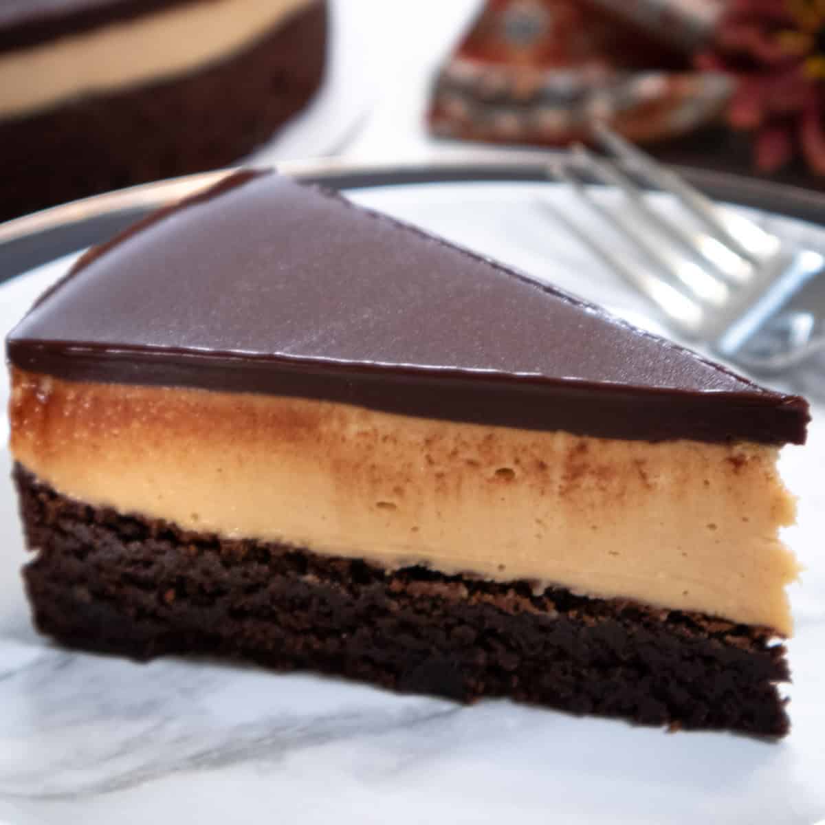 A slice of the Chocolate Peanut Butter Mousse Cake sits on a marlbe plate with the cake in the vackground along with a napkin.