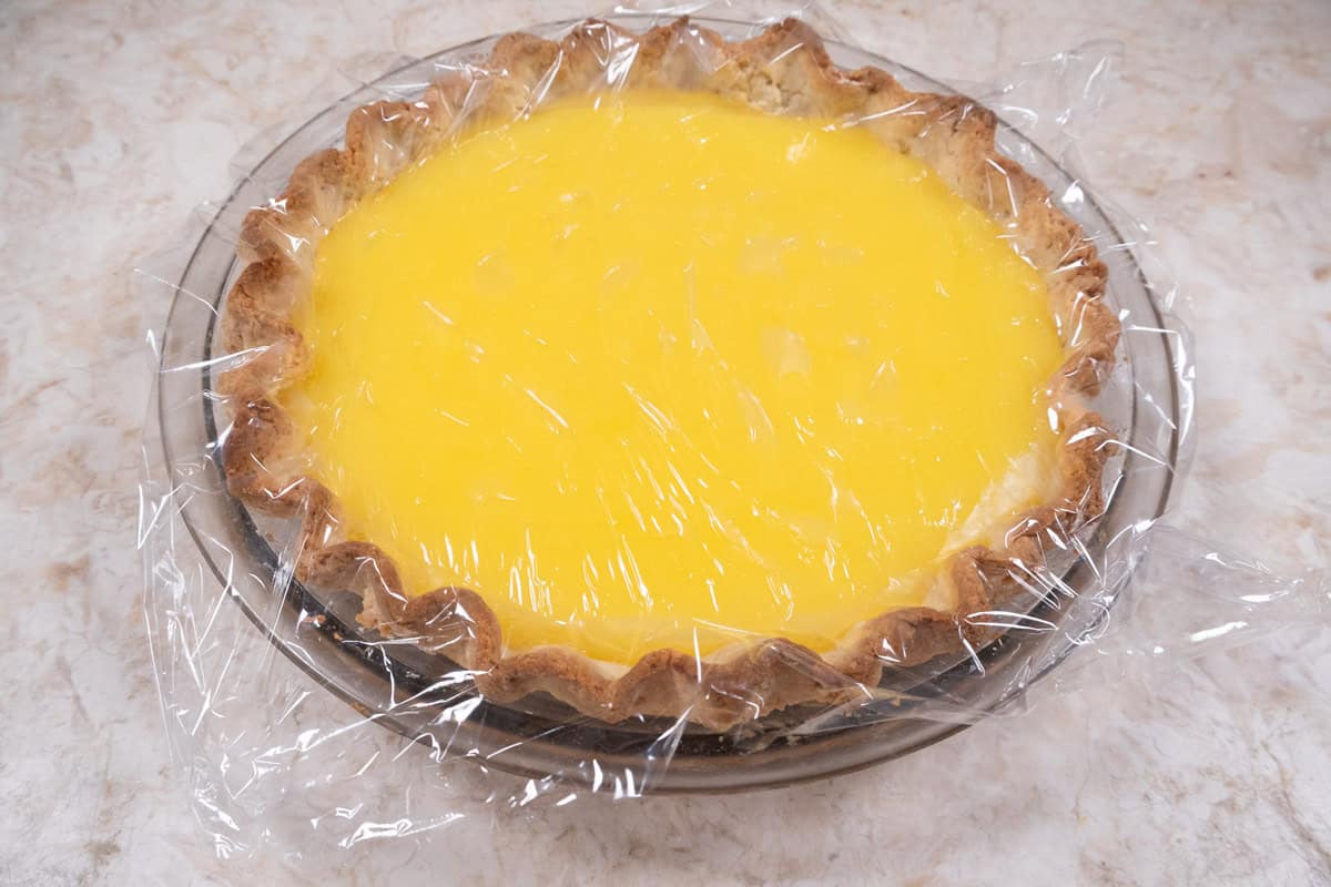 The filled pie crust is covered with plastic wrap while the filling cools.