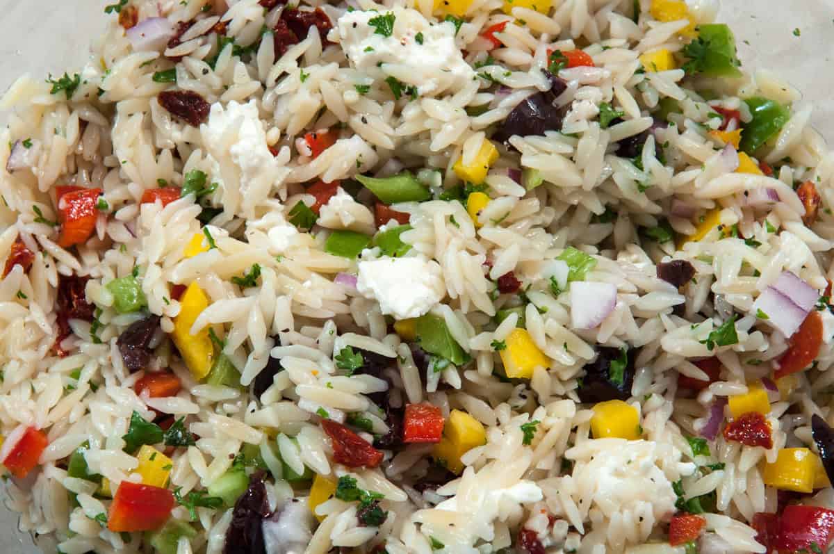A close up of the orzo salad with all of th e veggies, cheese and olives. 