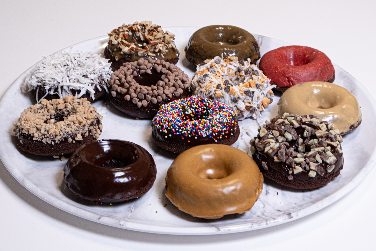 Chocolate Cake Donuts are featured with 12 different toppings sit on a marble platter.