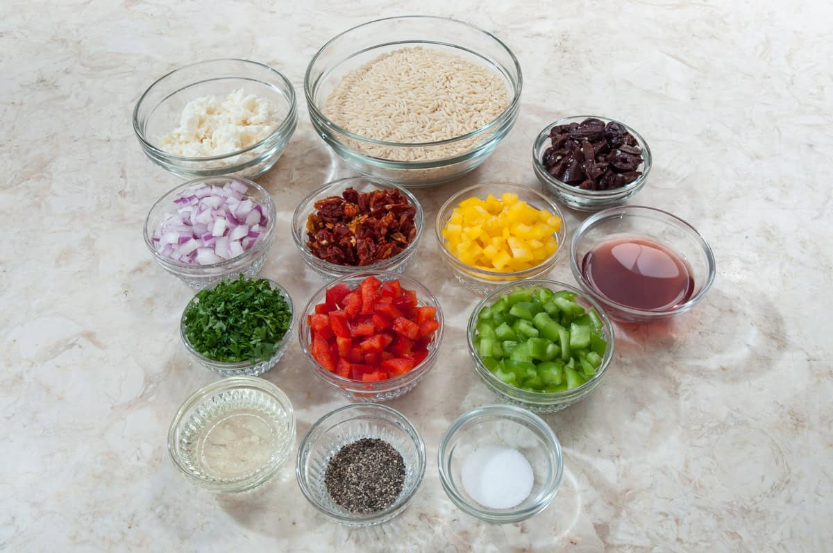 The Mediterranean Orzo ingredients include orzo, sundried tomatoes, feta cheese, red onion, yellow,  red and green peppers, parsley, calamata olives, red wine vinegar, olive oil, black pepper and salt. 