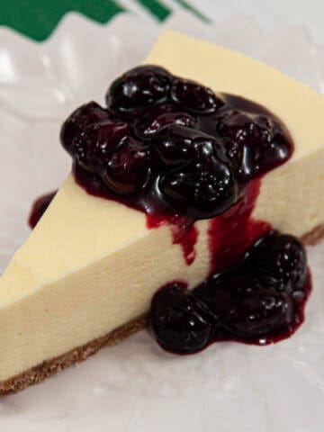 A slice of the Lemonade cake sits on a whit plate with a blueberry sauce.