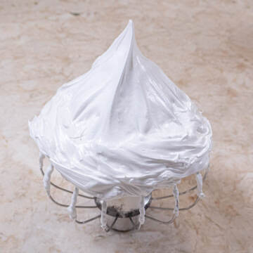 A whisk is upside down holding stiffly beaten meringue in a sharp peak.