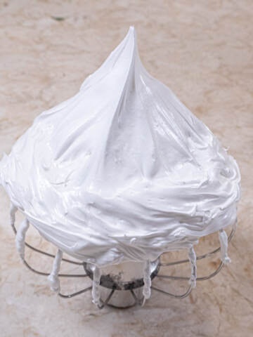 A whisk is upside down holding stiffly beaten meringue in a sharp peak.