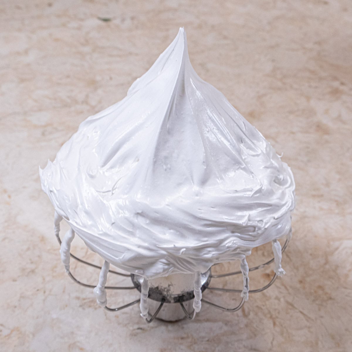 A whisk is upside down holding stiffly beaten meringue in a sharp peak.