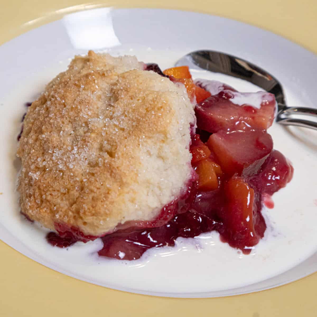 This photo for the Peach and Plum Cobbler shows the fruit in a bowl with a biscuit on top swimming in cream.