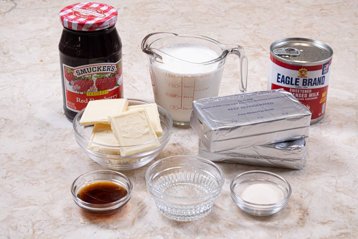 The ingredients for the cheesecake are: white chocolate, cream cheese, heavy cream, condensed milk, raspberry jam, and vanilla.