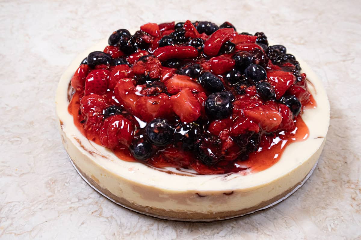 A whole cheesecake with the berry topping on a marble table.
