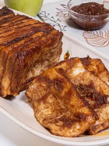 The Apple Cardamom Pull Apart Bread sits on a cream colored tray with an apple, apple butter, and cinnamon sticks in the background.