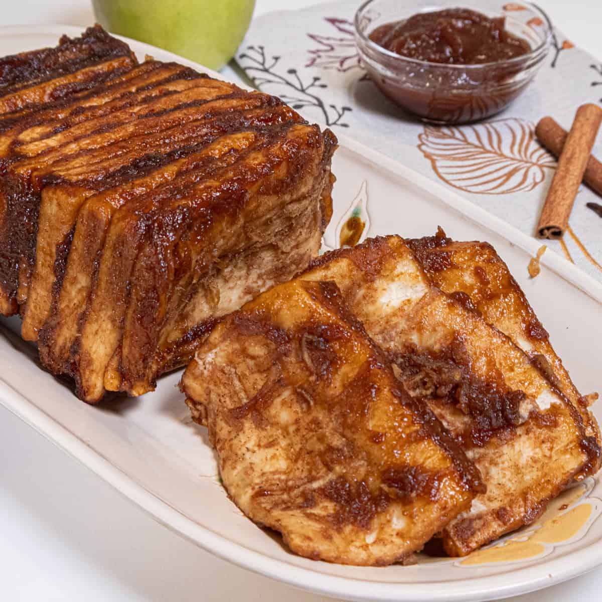The Apple Cardamom Pull Apart Bread sits on a cream colored tray with an apple, apple butter, and cinnamon sticks in the background.