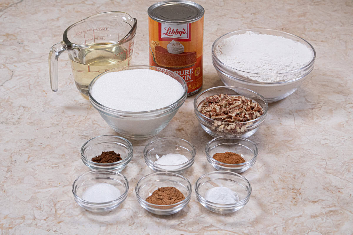 The Pumpkin Coffee Cake ingredients are granulated sugar, canola oil, eggs, canned pumpkin, salt, baking soda, baking powder, cloves, cinnamon, nutmeg, all-purpose flour, and chopped pecans