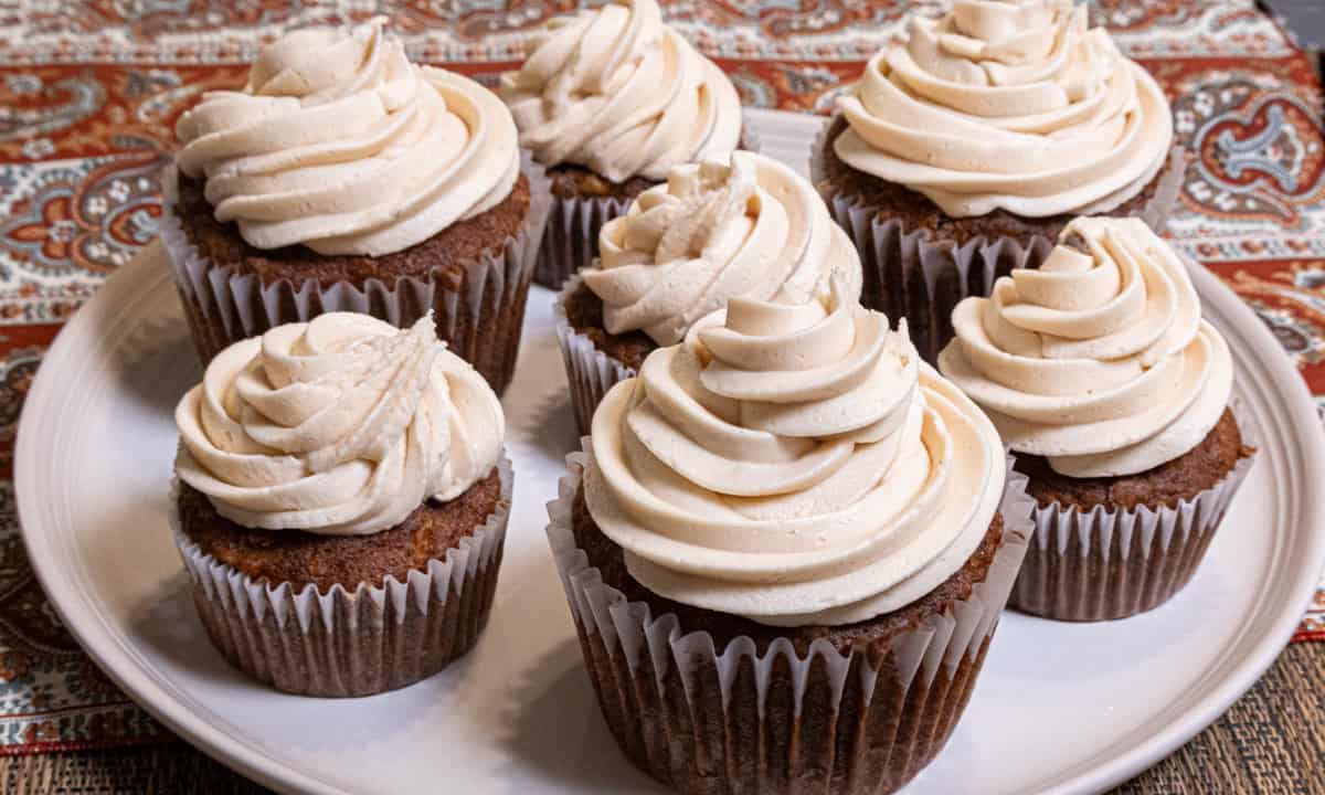This is avphoto of six cupcakes on a cream colored plate. 