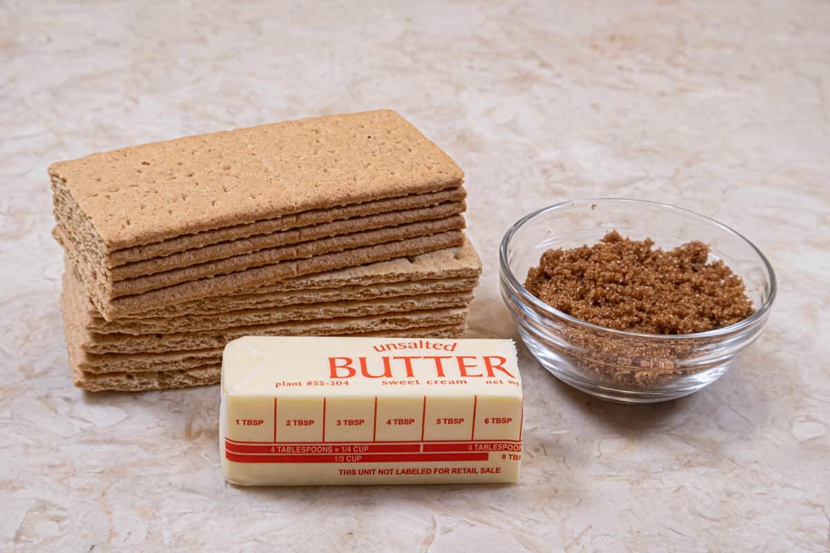 The ingredients for the Caramel Pecan Cheesecake crust are graham crackers, brown sugar, and unsalted butter